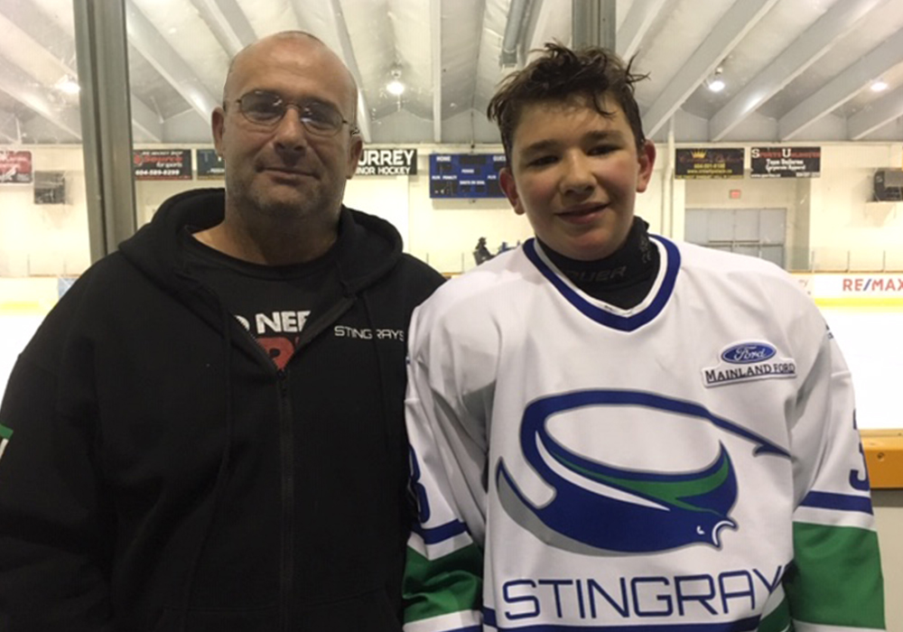 Father and son pose at hockey rink for a photo.